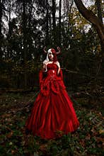 Maleficent Woman in Red Clothing and Horns in dark Forest. Posing in magik forest