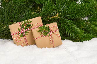 Two handmade plastic-free Christmas presents under fir tree. Gifts wrapped in craft paper and rope bow in snow with green pine