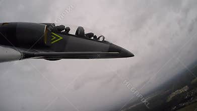 A gray blue training fighter aircraft flying against a dark overcast cloudy day. The navigator gestures and gives signals