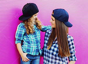 Portrait of young mother with child little girl wearing a checkered shirts and baseball cap in city over pink