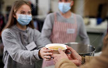 Volunteers serving hot soup for homeless in community charity donation center, coronavirus concept.