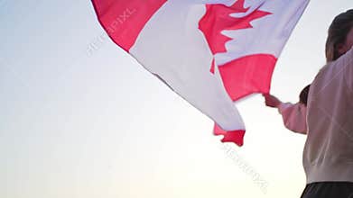A woman runs with the flag of Canada against a clear sky. Patriotism of citizen of Canada