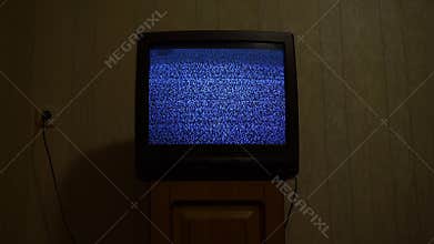Old retro tv with glitch snowy broadcast stands on wooden bedside table