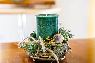 Green candle decorated for Easter with flowers, feathers and eggs.