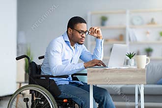 Focused young man in wheelchair using laptop computer for online work or communication at home