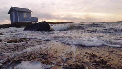 Blue bath cabin and waves breaking against beach at sunset