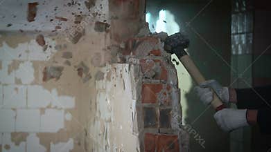 A worker with a sledgehammer demolishes a brick wall. The concept of overcoming obstacles in life and work.