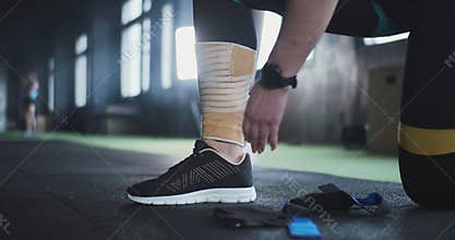 Sports medicine and technology. Close-up female athlete puts elastic knee wrap tape on leg, preparing for gym workout.