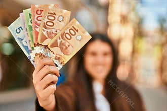 Young hispanic woman smiling happy holding canadian dollars at the city