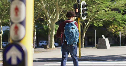 African american man in city, carrying backpack crossing street