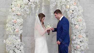 beautiful and happy bride and groom exchange rings in an arch of flowers