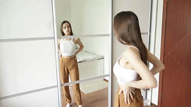 Weight loss. Teen girl at home in front of the mirror examines the waist after dieting