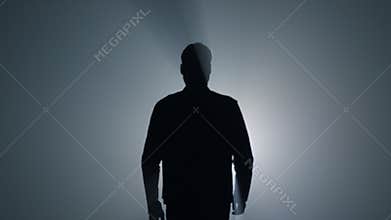 Silhouette man going away in dark background. Back view guy walking in darkness.