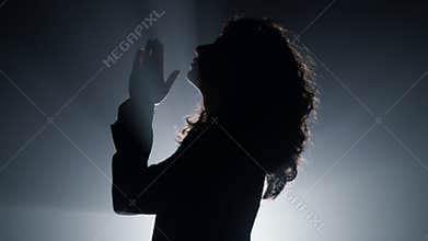 Silhouette woman praying in darkness. Believer girl whispering prayer indoors.