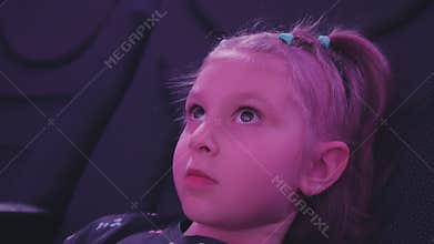 A little girl sitting in the planetarium auditorium looks up and laughs.