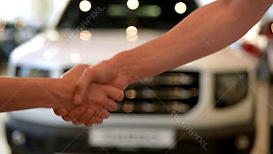Side view of unrecognizable female buyer handing cash to car salesman and shaking hands in car dealership. Process new