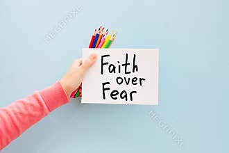 Faith over fear - woman hand with christian motivational text on light blue background