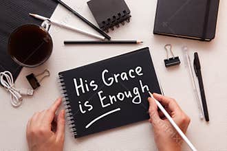 His grace is enough - woman hands with christian motivational text with black and white stationery on the table