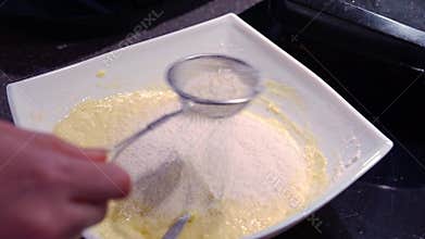 A woman&#x27;s hand mixes the dough with the added flour with a spoon.