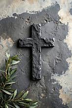 A stone cross on a concrete wall next to a branch of olive