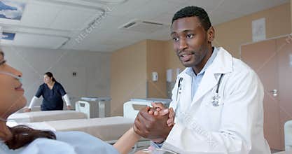 Diverse male doctor holding hand of female patient with oximeter in hospital bed, slow motion