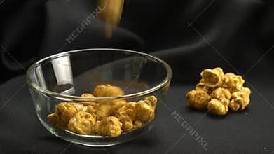 Drop sweet caramel almonds into transparent glass bowl.