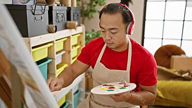 Handsome young chinese man, an aspiring artist, engrossed in drawing while listening to soulful music in an indoor art studio