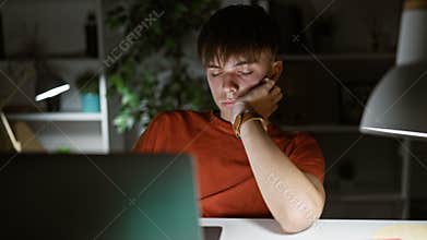 A young caucasian male spends a late night working on a computer in a dark home office