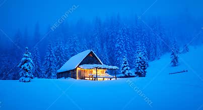 A wintery scene in the heart of the woods with a solitary wooden cottage