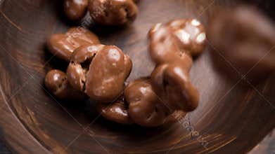 Chocolate covered walnut. Delicious nutritious nut candies falling into a rotating wooden bowl