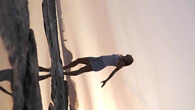 Vertical video, Girl tossing volleyball up by the sea at sunset.