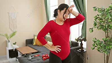 Hispanic woman in red sportswear posing confidently indoors for a fitness-related shoot, with home workout equipment in the