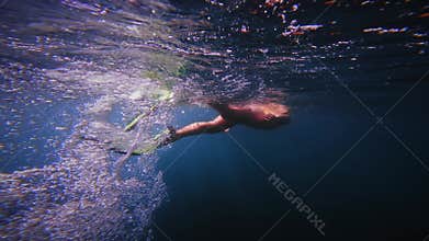 Woman freediver with fins dive to sea bottom. Freediving in blue ocean with sun rays