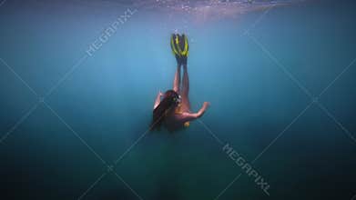 Woman freediver with fins dive to sea bottom. Freediving in blue ocean with sun rays