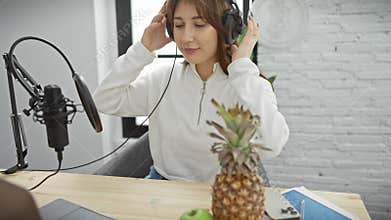 A young woman podcasting in a modern studio with microphone, laptop, and fruits