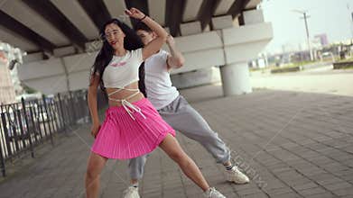 A young couple dances a street dance under a city bridge on a summer day outdoors. Contemporary energetic street dance.