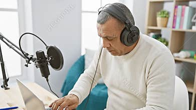 Mature hispanic man podcasting in a home studio, focused while adjusting a microphone and wearing headphones