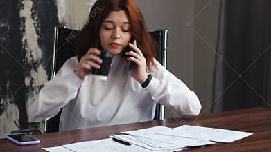 Frustrated caucasian woman employee speaking mobile phone at desk. Stressed woman check papers talking client on call