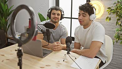 Two men podcasting with microphone and laptop in modern radio studio