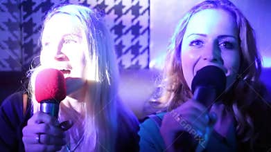 Two women singing into a microphone sitting at a