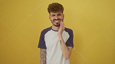 Young hispanic man with painful toothache, a dramatic portrait of dental illness expression, hand touching aching tooth, standing
