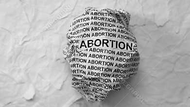 Crumpled paper ball with words Abortion on a torn white paper pieces background.