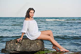 Caucasian teen girl in bikini and white shirt lounging on lava rocks by the ocean