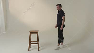 A dynamic dance pose is masterfully performed on a stool in a minimalist setting