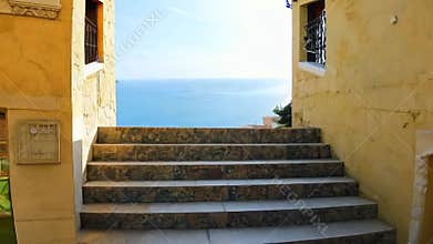 A shot of a set of stairs leading to a view of the ocean. The stairs are made of stone and are framed by the walls of a yellow bu