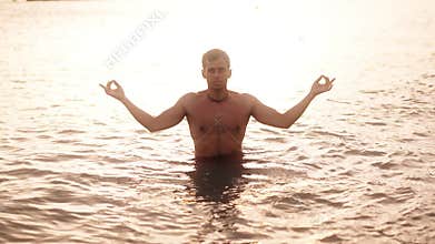 A person meditates in serene waters as the sun sets