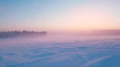 Pastel pink and blue sky over a field of undisturbed snow, a line of trees barely visible in the background through a