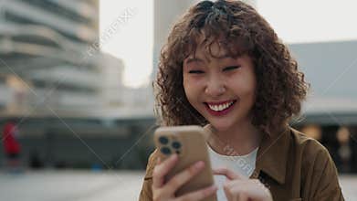 Excited Asian Girl Celebrates Online Achievement Standing In City Center With Cell Phone In Hand.