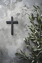 A black cross on a concrete wall next to a branch of olive branches