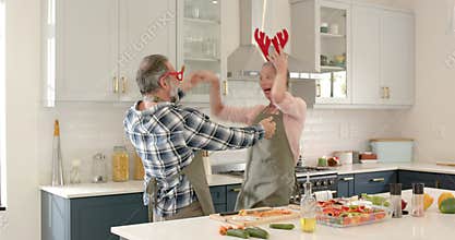 At Christmas, Mature couple dancing joyfully in kitchen wearing festive antler headbands